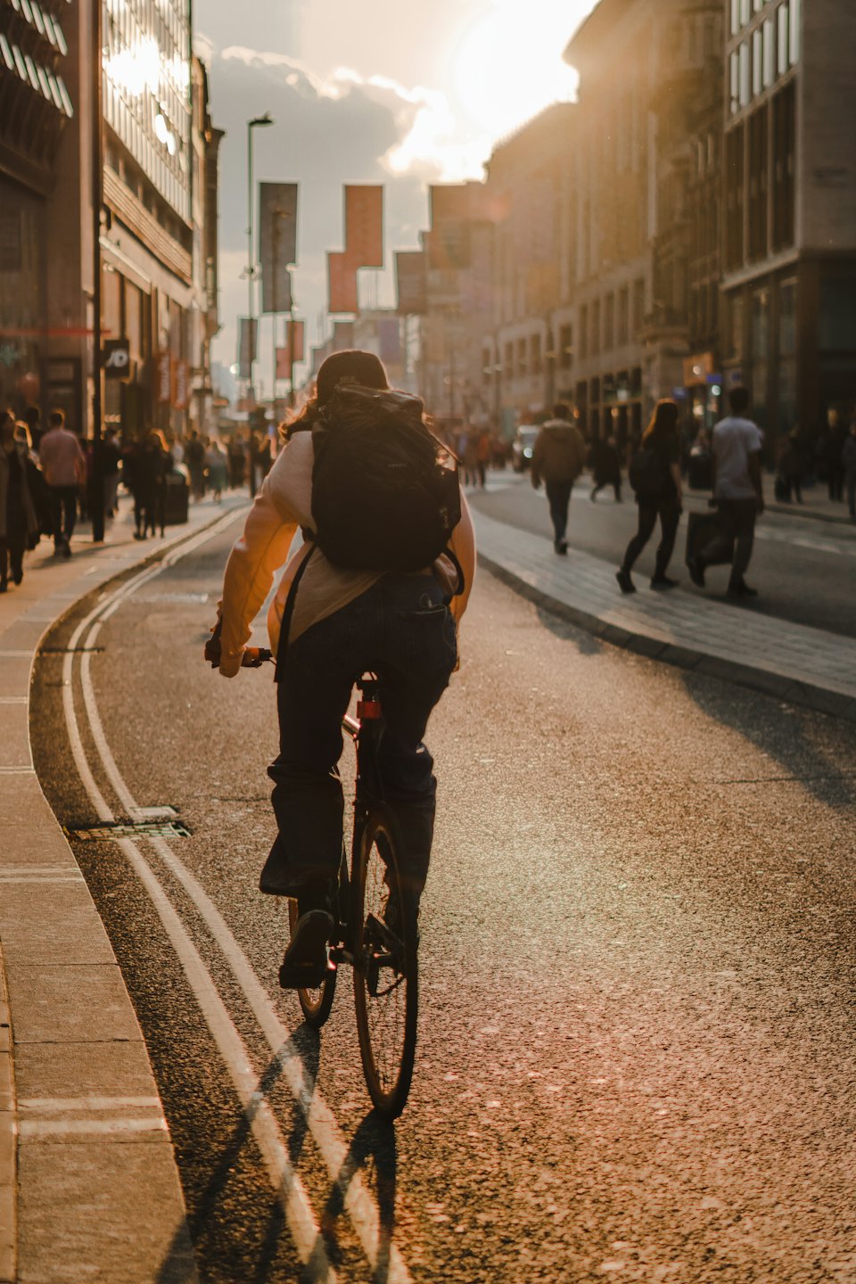 Person on bicycle rides down busy city street at sunset.