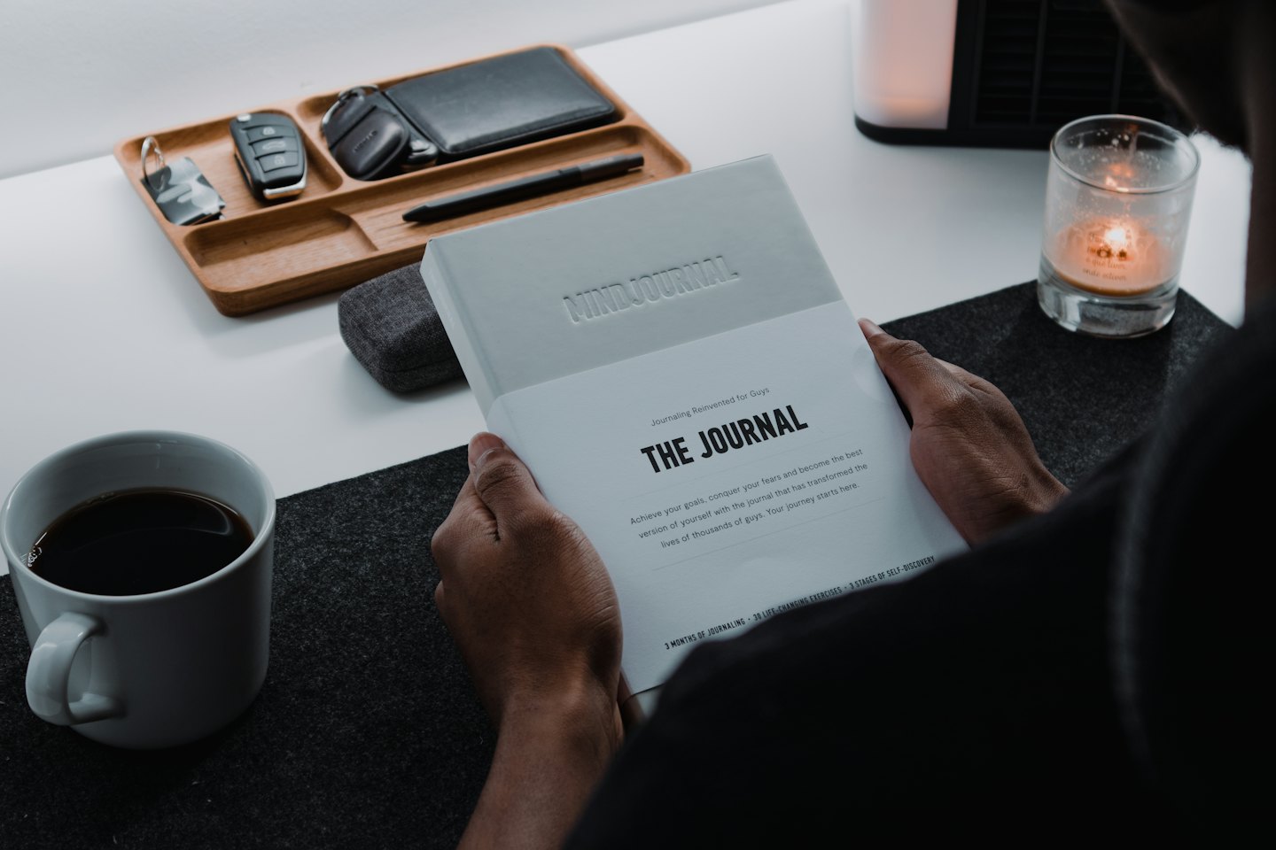 Hands holding a MINDJOURNAL at a desk with a wallet and coffee mug.